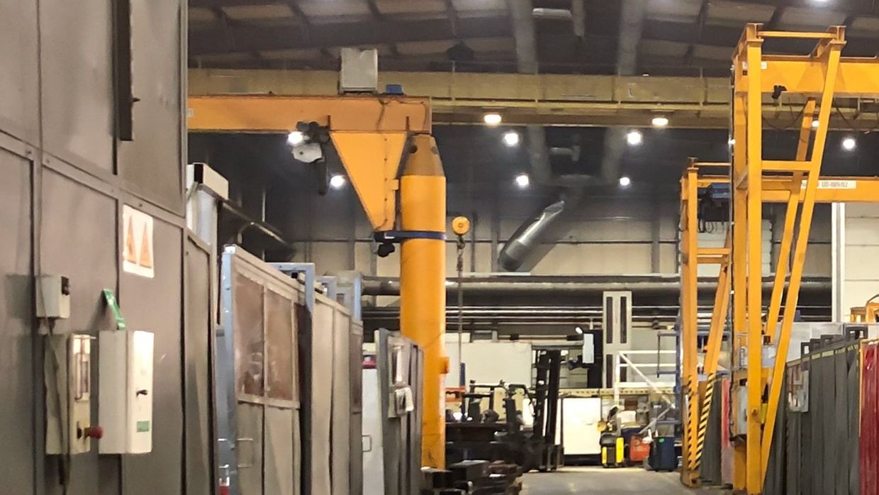 Grúa pluma de columna con brazo giratorio y polipasto sirviendo un puesto de trabajo en una nave industrial