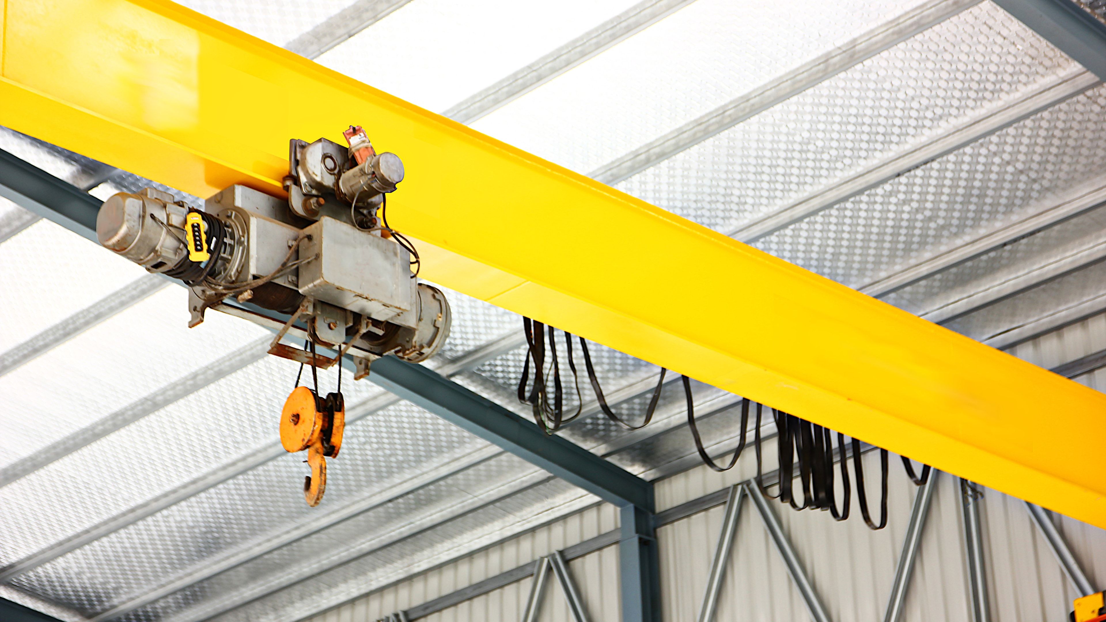 Puente grúa monorraíl instalado en nave industrial: viga amarilla con polipasto eléctrico de cable y gancho