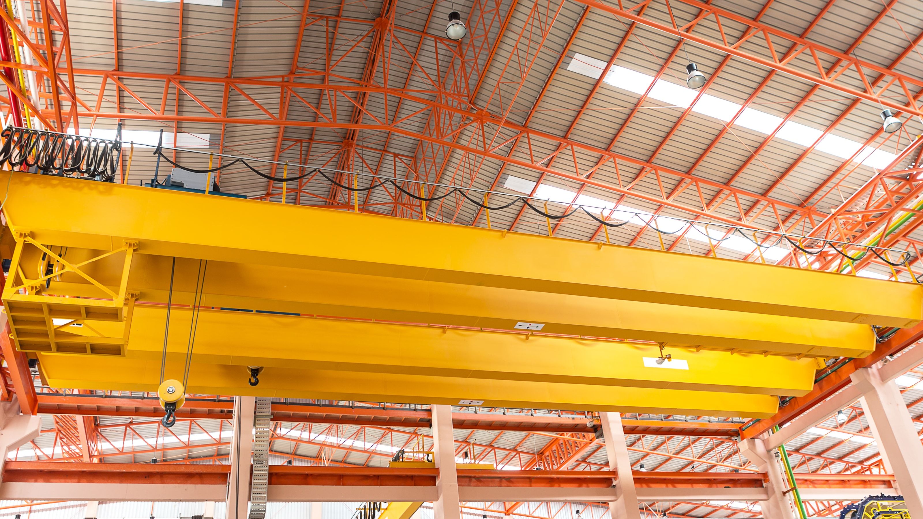 Puente grúa en el interior de una nave industrial: puente birrail amarillo con gancho bajo cerchas de acero